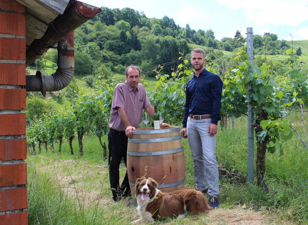 Markus Dobler und Andreas Dobler mit Hund Benno am Barriquefass in den Weinbergen