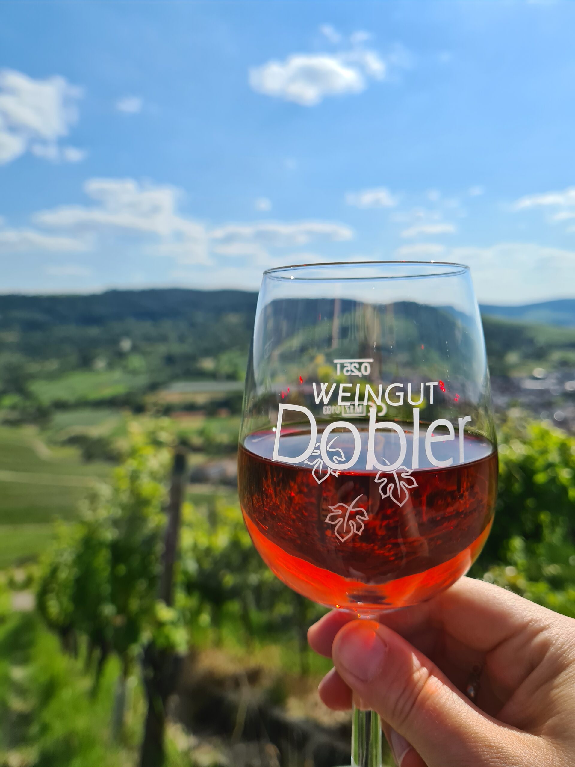 Weinglas mit Roséwein, im Hintergrund sind Weinberge und das Remstal zu sehen